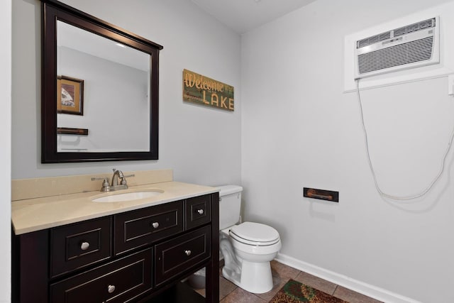 half bathroom with toilet, a wall mounted air conditioner, vanity, tile patterned flooring, and baseboards