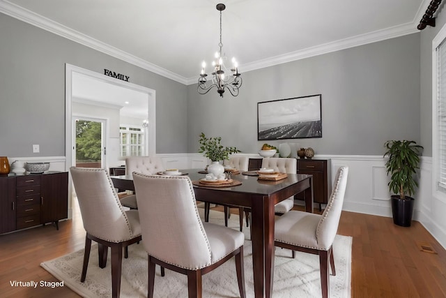 dining room with ornamental molding, an inviting chandelier, a wainscoted wall, and wood finished floors