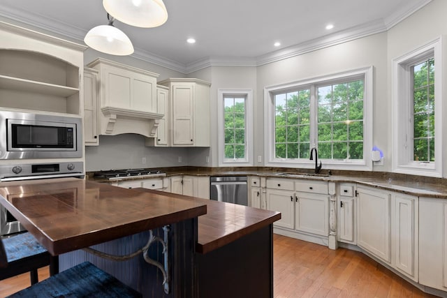 kitchen with a sink, stainless steel appliances, butcher block counters, light wood-type flooring, and a breakfast bar area