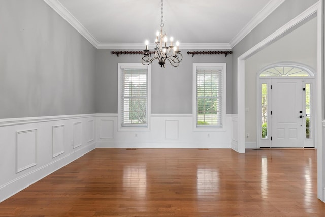 interior space featuring an inviting chandelier, crown molding, a wainscoted wall, and wood finished floors