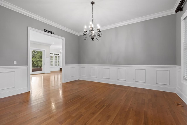 empty room with a wainscoted wall, wood finished floors, ornamental molding, visible vents, and a notable chandelier