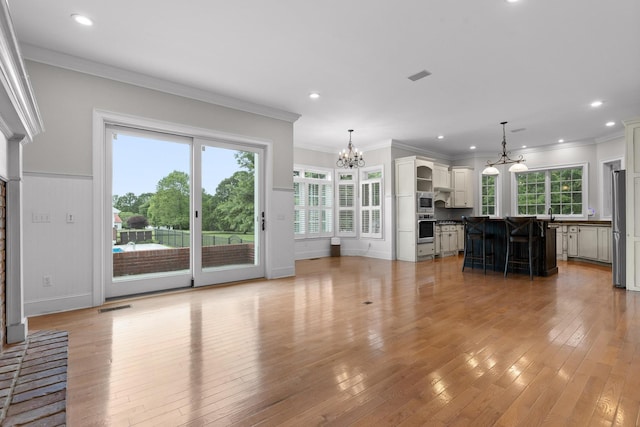 unfurnished living room featuring a wealth of natural light, a notable chandelier, light wood-style flooring, and visible vents