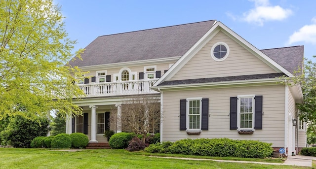 view of front of house featuring a porch, a shingled roof, a front lawn, and a balcony