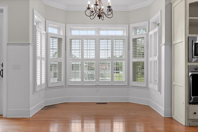 unfurnished dining area featuring ornamental molding, a notable chandelier, light wood-style flooring, and baseboards