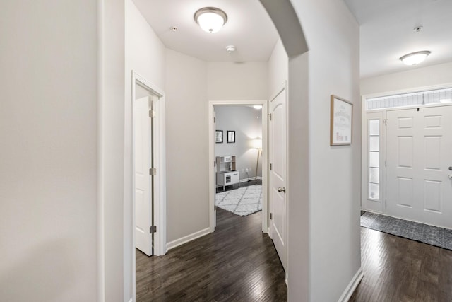 foyer entrance with arched walkways, dark wood-style flooring, and baseboards