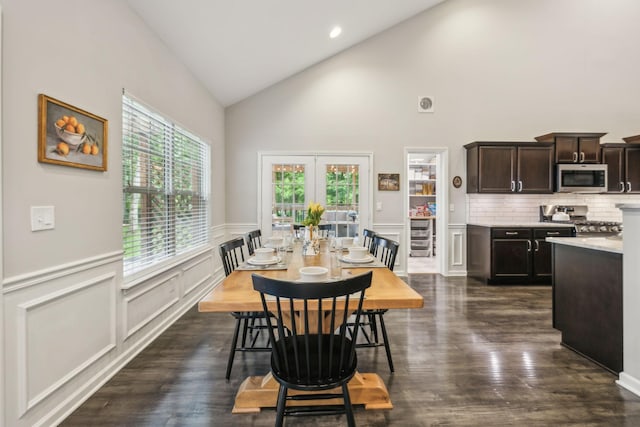 dining room with dark wood-style floors, a decorative wall, high vaulted ceiling, and a wainscoted wall