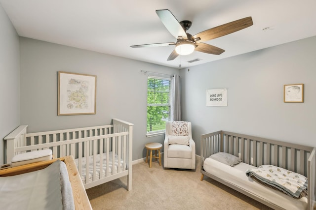 bedroom featuring a nursery area, carpet, visible vents, and a ceiling fan