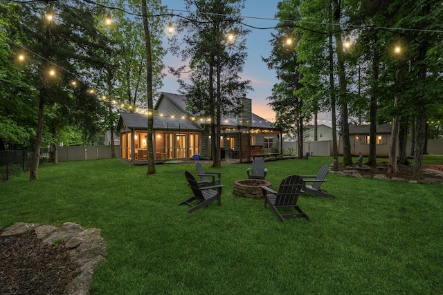yard at dusk featuring a fenced backyard, an outdoor fire pit, and a sunroom