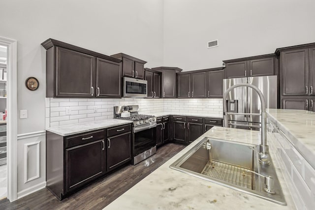 kitchen featuring stainless steel appliances, dark brown cabinets, visible vents, and a towering ceiling