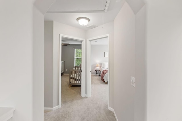 hall with light carpet, attic access, baseboards, and visible vents