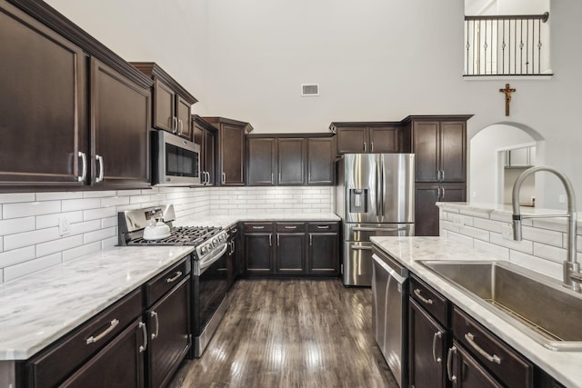 kitchen with a sink, visible vents, dark brown cabinetry, decorative backsplash, and appliances with stainless steel finishes