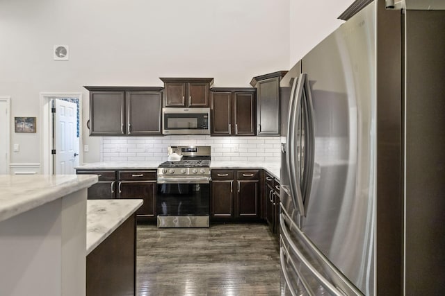 kitchen with decorative backsplash, dark wood-style floors, light stone countertops, dark brown cabinets, and appliances with stainless steel finishes