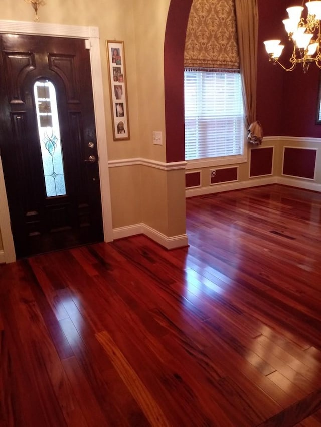 entryway with arched walkways, baseboards, a notable chandelier, and wood finished floors