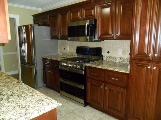 kitchen with appliances with stainless steel finishes, tasteful backsplash, light stone countertops, and ornamental molding