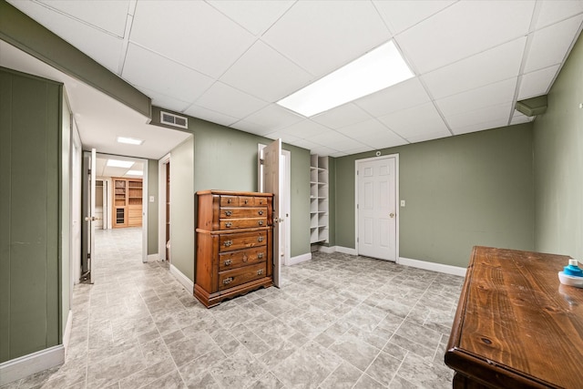 interior space with baseboards, a drop ceiling, stone finish flooring, and visible vents