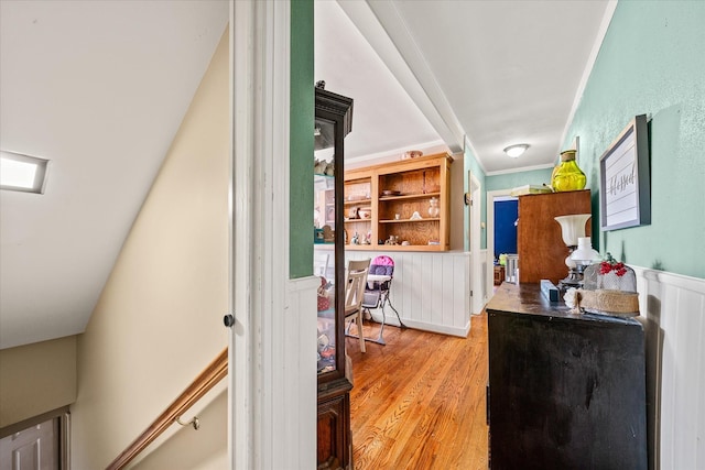 hall with a wainscoted wall, crown molding, and light wood-type flooring