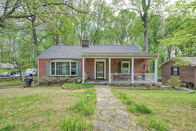 single story home featuring covered porch, roof with shingles, brick siding, a front yard, and a chimney