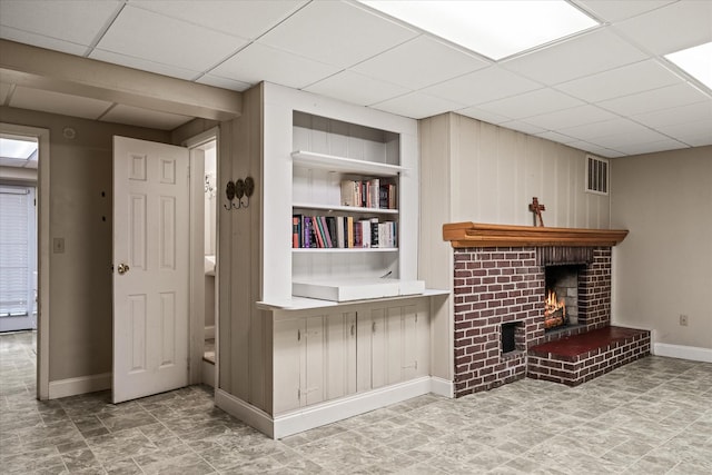 living area with a fireplace, a paneled ceiling, built in features, baseboards, and visible vents