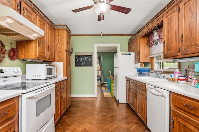 kitchen with under cabinet range hood, brown cabinetry, white appliances, and a sink