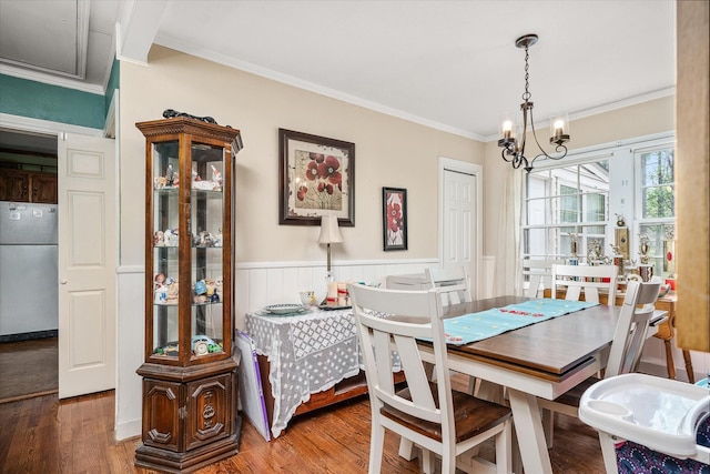 dining area featuring crown molding, wood finished floors, a wainscoted wall, and a notable chandelier