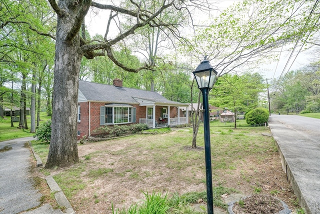 view of front of home featuring a porch, brick siding, a front yard, a chimney, and a shingled roof