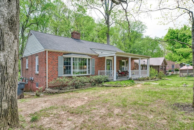 view of front of home with covered porch, a chimney, a shingled roof, a front yard, and brick siding