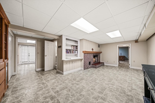 unfurnished living room with a drop ceiling, stone finish flooring, a fireplace, visible vents, and baseboards