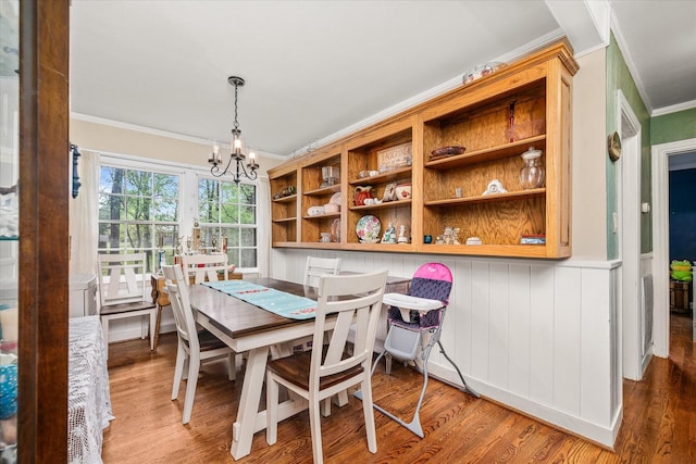 dining space with crown molding, wood finished floors, a wainscoted wall, and a notable chandelier