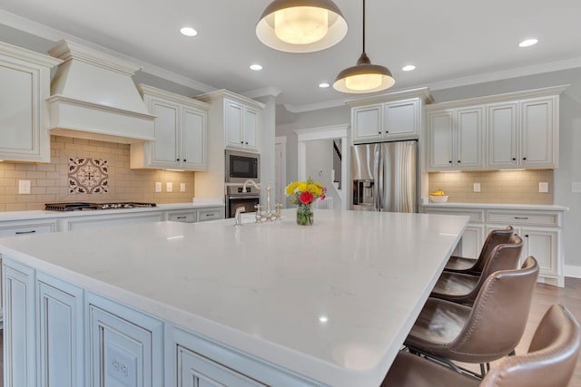 kitchen with custom range hood, crown molding, stainless steel appliances, tasteful backsplash, and a large island with sink