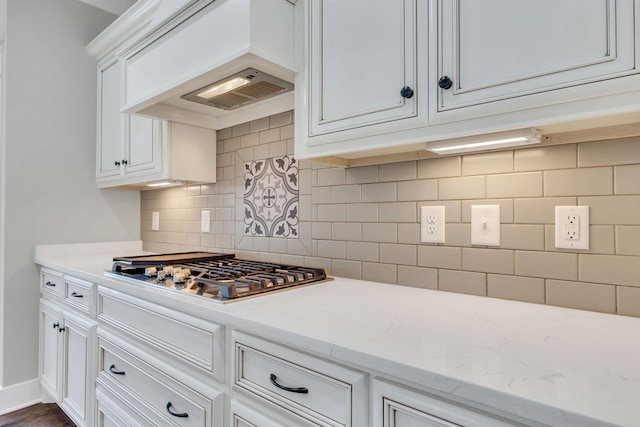 kitchen with light stone countertops, stainless steel gas stovetop, white cabinetry, premium range hood, and decorative backsplash