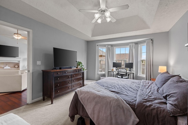 bedroom with a tray ceiling, carpet floors, a textured ceiling, baseboards, and ceiling fan