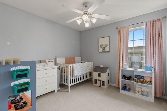 bedroom featuring a ceiling fan, light carpet, a crib, and baseboards