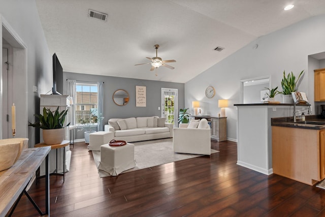 living area with a ceiling fan, dark wood finished floors, visible vents, and vaulted ceiling