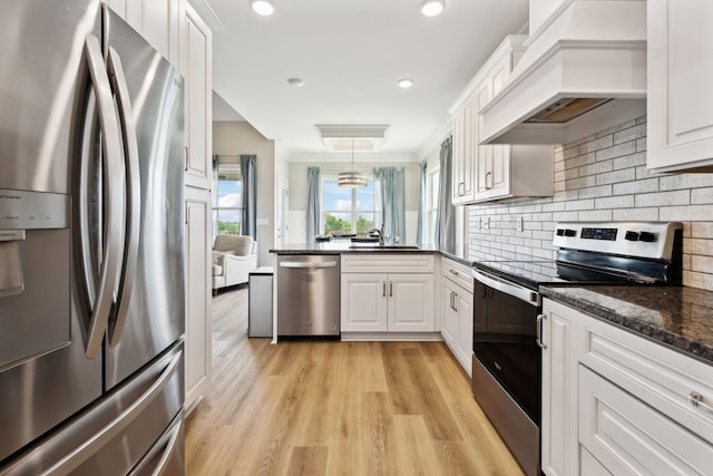 kitchen with premium range hood, appliances with stainless steel finishes, white cabinetry, decorative backsplash, and light wood-style floors