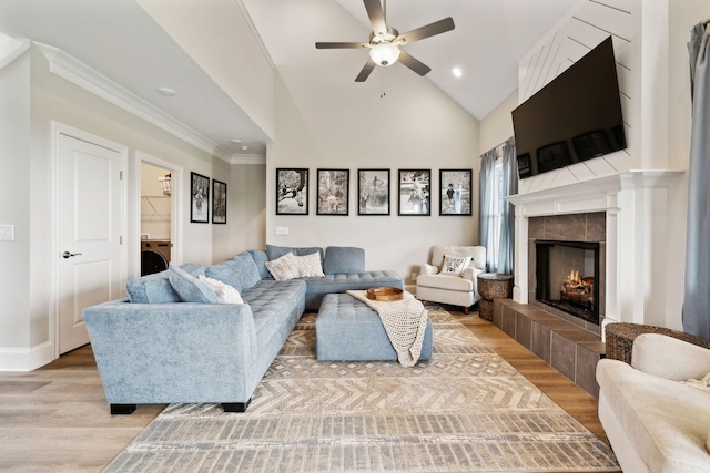 living room featuring washer / clothes dryer, light wood-style flooring, ceiling fan, crown molding, and a fireplace