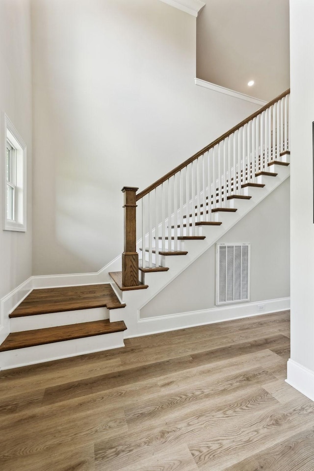 staircase with crown molding, baseboards, visible vents, and wood finished floors