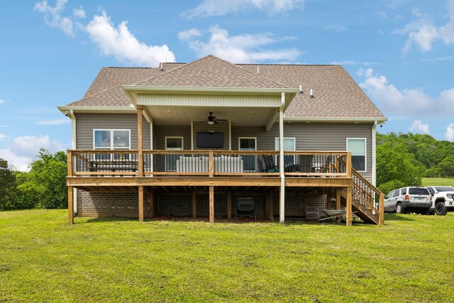 back of house with a ceiling fan, a deck, roof with shingles, and a lawn