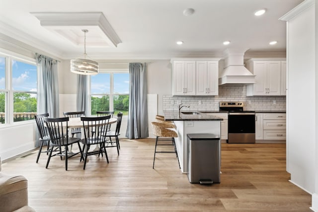 kitchen featuring premium range hood, a sink, a kitchen bar, white cabinets, and stainless steel range with electric cooktop
