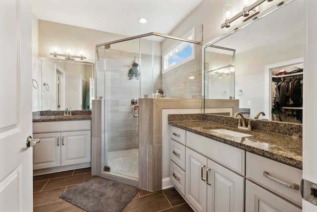 bathroom featuring a sink, a walk in closet, two vanities, and a stall shower