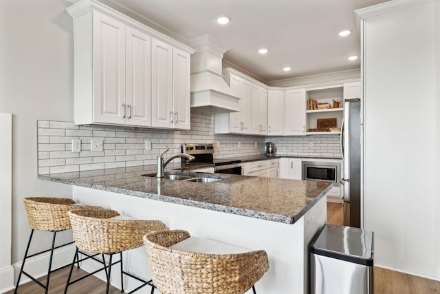 kitchen featuring a peninsula, a sink, open shelves, white cabinets, and appliances with stainless steel finishes