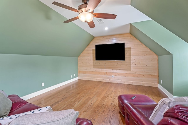 living room with lofted ceiling, a ceiling fan, baseboards, visible vents, and wooden walls