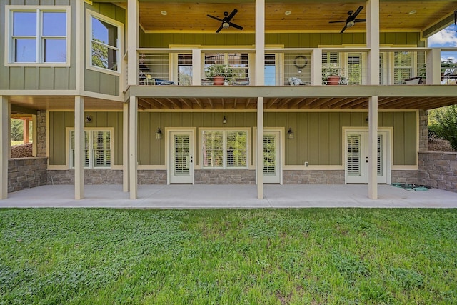 rear view of house with ceiling fan, a lawn, stone siding, and board and batten siding