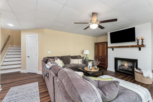 living room featuring stairway, ceiling fan, dark wood-style flooring, a large fireplace, and a paneled ceiling