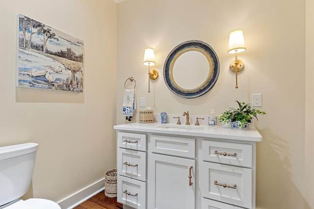 half bath with toilet, baseboards, vanity, and wood finished floors