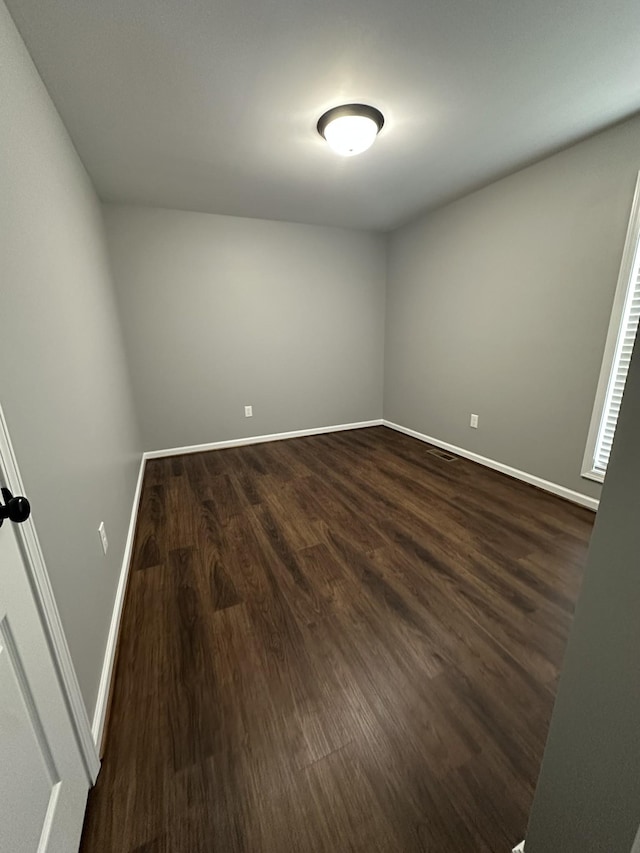 spare room featuring baseboards and dark wood-type flooring