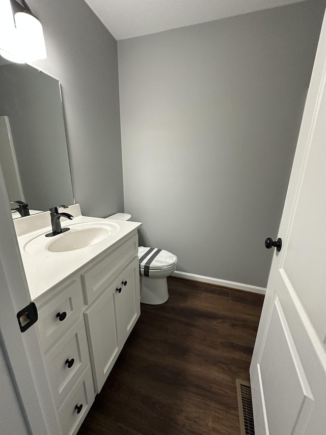 bathroom featuring toilet, wood finished floors, vanity, visible vents, and baseboards