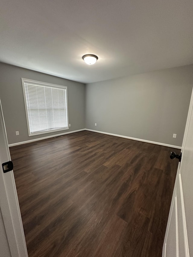 empty room with dark wood-type flooring and baseboards