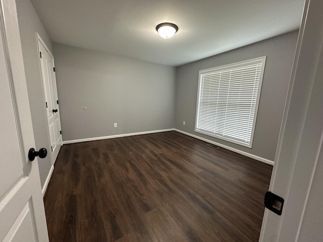 unfurnished room featuring dark wood finished floors, visible vents, and baseboards