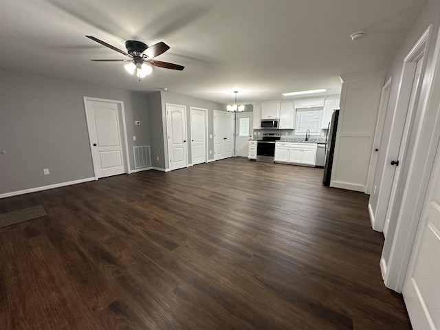 unfurnished living room featuring a sink, ceiling fan with notable chandelier, visible vents, dark wood-style flooring, and baseboards
