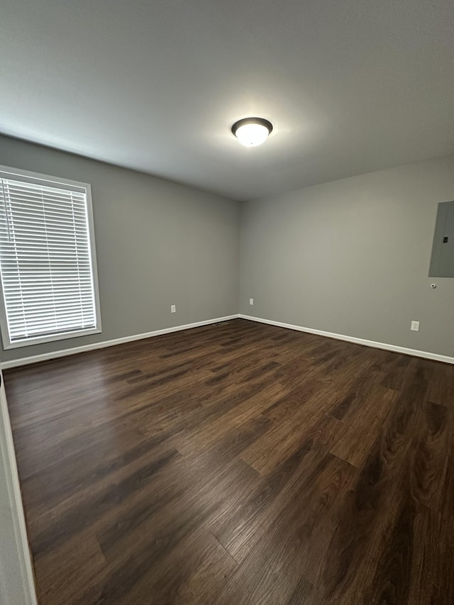 spare room featuring baseboards, electric panel, and dark wood-type flooring